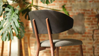 Détail d'une chaise Mobitec Toro en bois foncé à assise grise devant un mur en briques