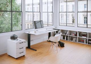 Lifestyle image of a white Buronomic Comfort pedestal under a black desk by large windows