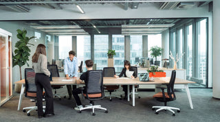 Sfeerbeeld van teams aan König + Neurath CONNECT.BENCH tafels in een open kantoor met glazen gevel